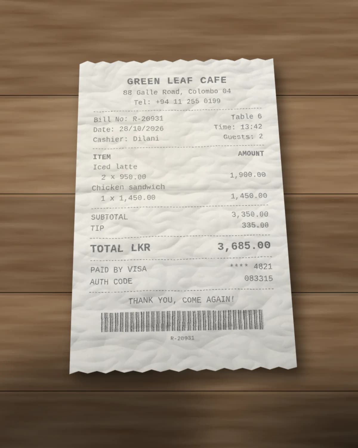 Phone photo of a crumpled Green Leaf Cafe thermal receipt on a wooden table: bill R-20931 on 28/10/2026 at 13:42, 2 iced lattes and a chicken sandwich, tip 335.00, total LKR 3,685.00 paid by Visa ending 4821
